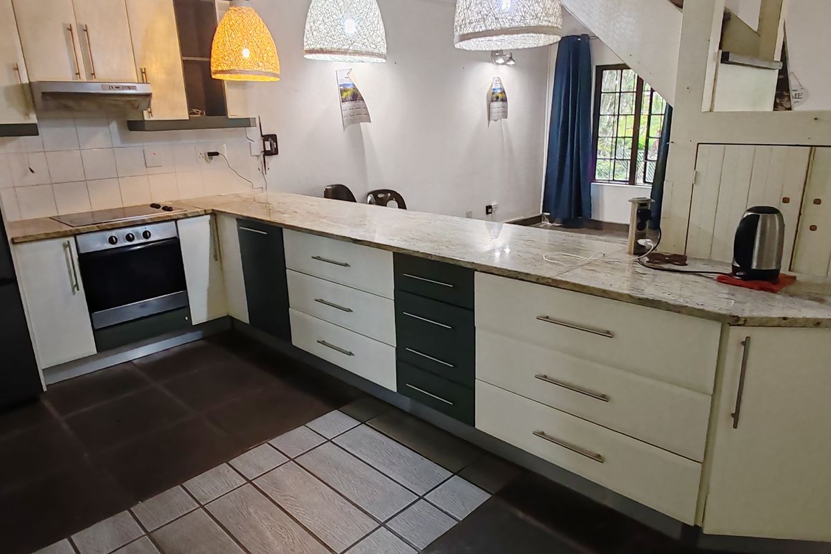 A functional kitchen featuring a long stone countertop, built-in oven, extractor fan, and a mix of white and dark cabinetry.