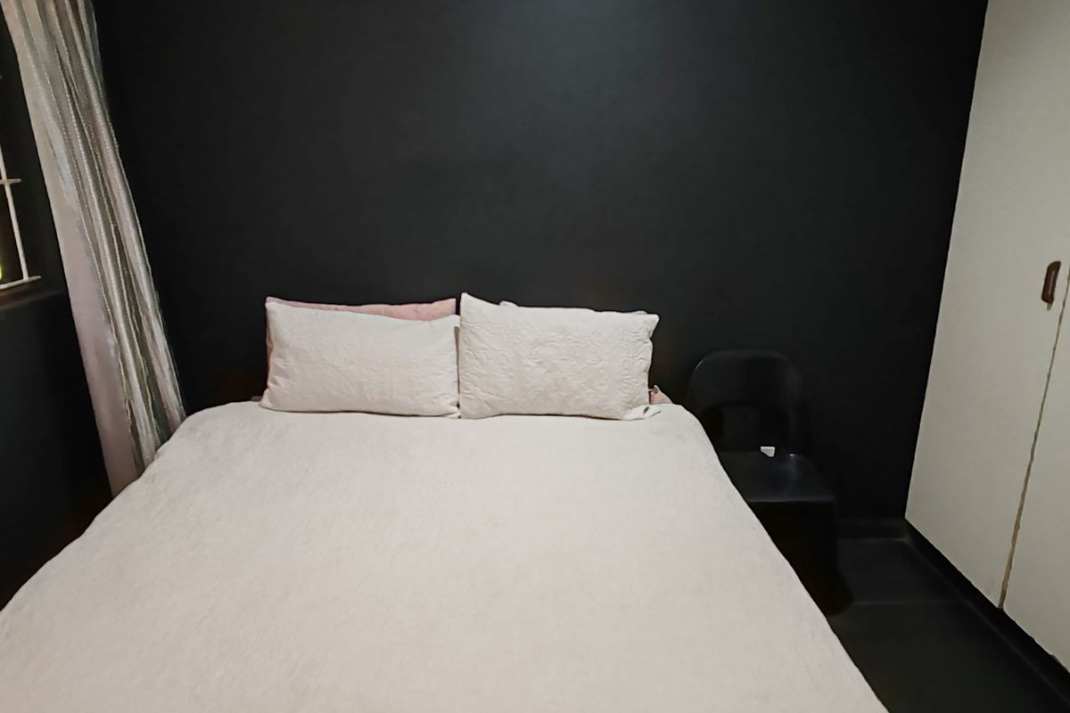 A bedroom featuring a dark accent wall, built-in wardrobe storage, and a window with security bars.