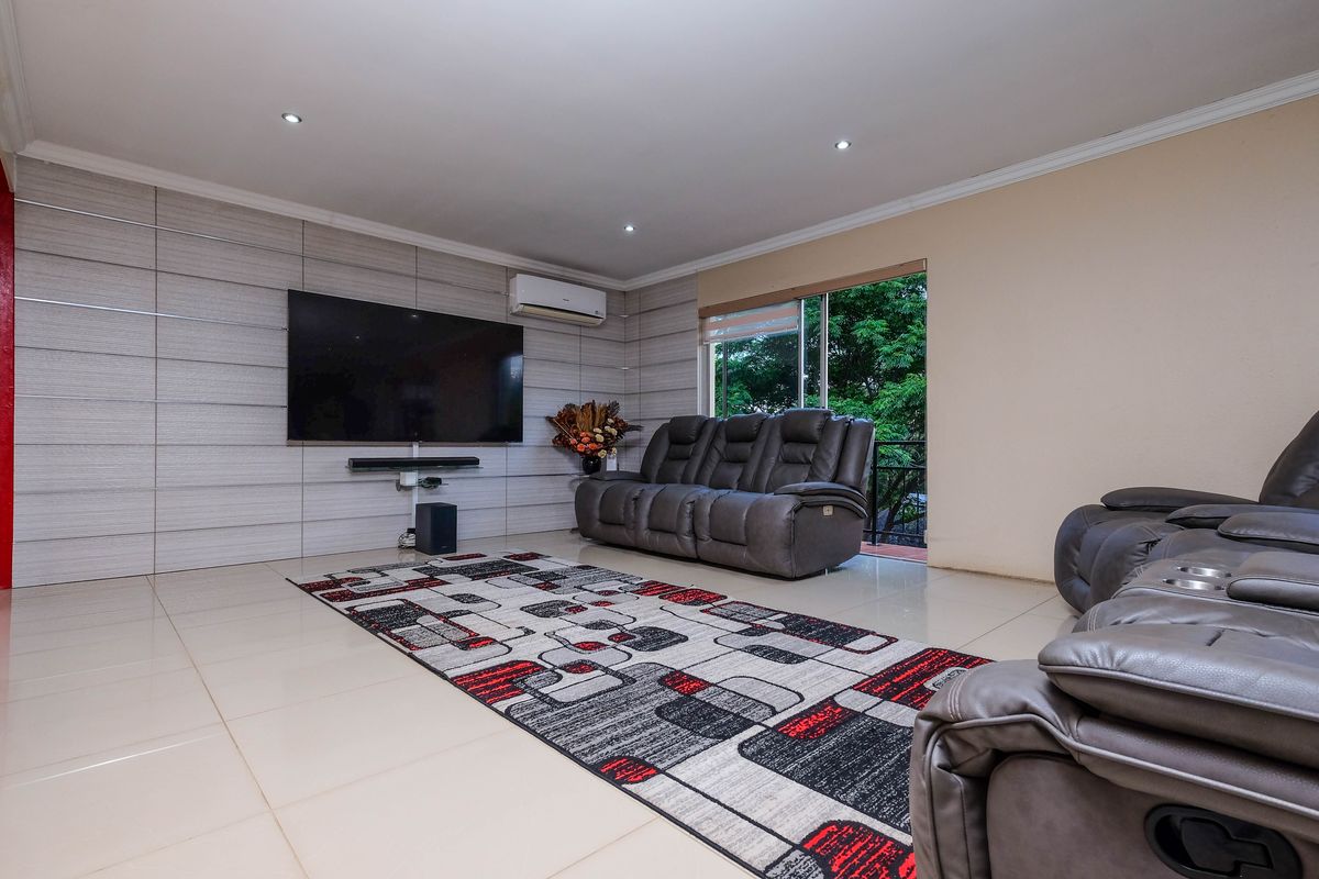 Spacious living room featuring tiled flooring, recessed ceiling lighting, a wall-mounted air conditioning unit, and a feature wall with integrated media setup.
