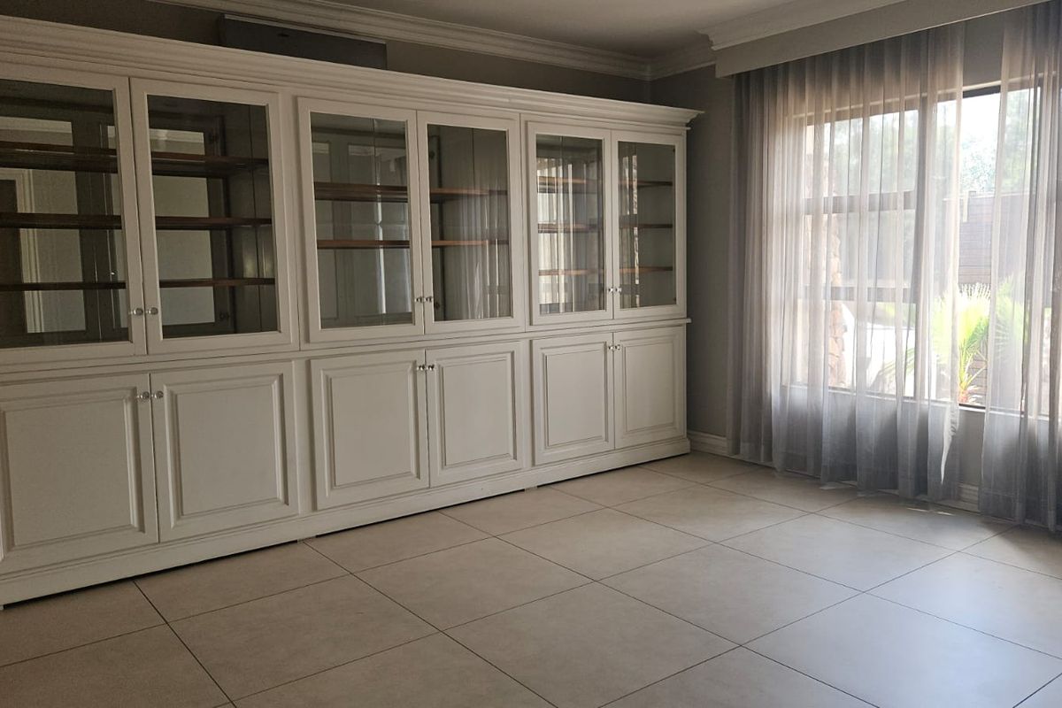 A bright living area featuring large format floor tiles and a substantial, custom-built white cabinetry unit with glass display shelving.