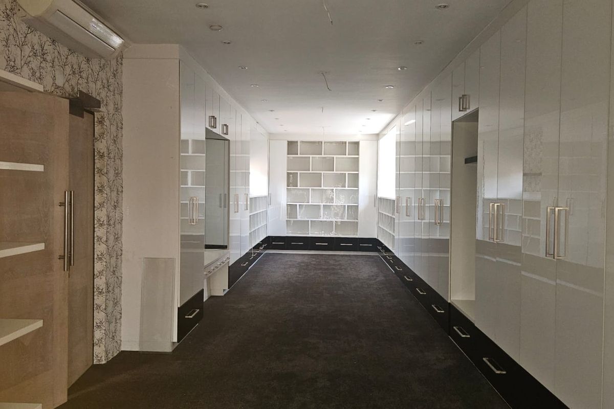 A spacious walk-in dressing room featuring extensive floor-to-ceiling white cabinetry, integrated shelving, recessed lighting, and a wall-mounted air conditioning unit.