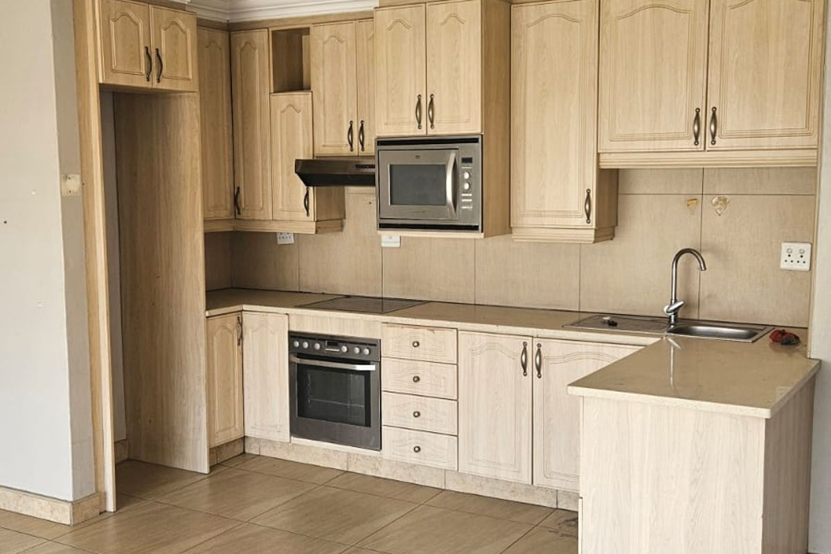 A functional kitchen featuring light wood-tone cabinetry, built-in oven, hob, extractor fan, and integrated microwave, complemented by tiled flooring and a peninsula counter.