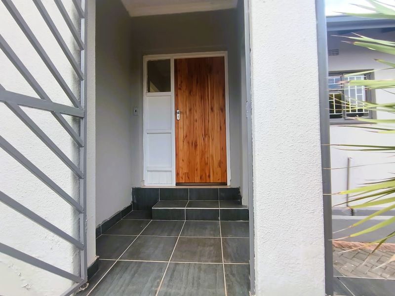 A clean and well-maintained entrance area featuring a solid wooden front door, tiled steps, and a secure metal gate.