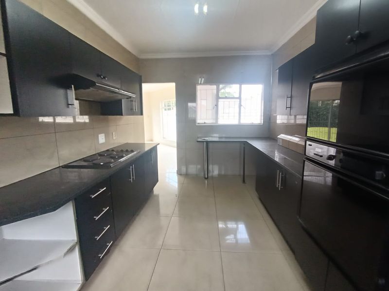 A functional kitchen featuring dark built-in cabinetry, granite countertops, a built-in oven and hob, and tiled flooring throughout.