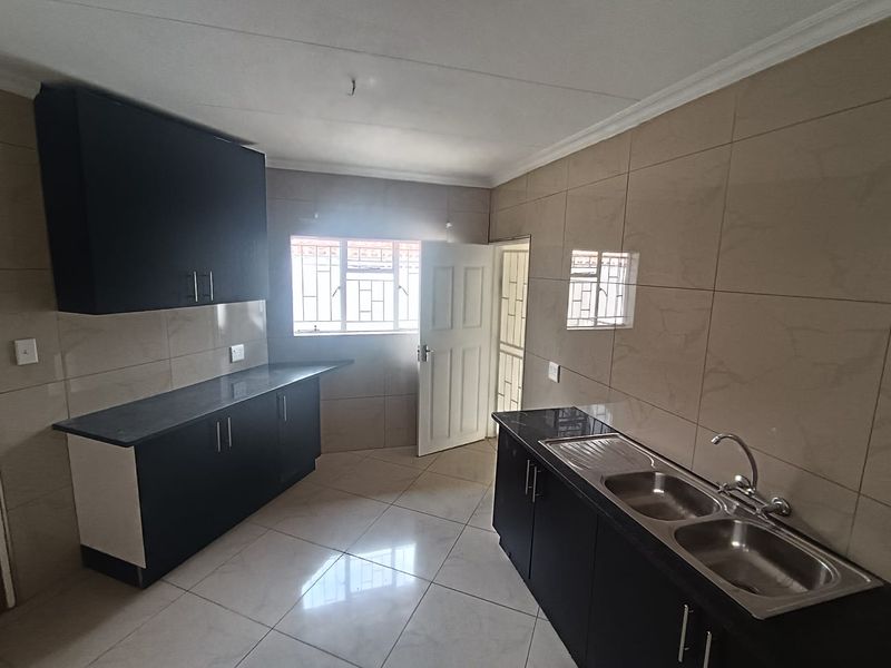 A clean, modern kitchen featuring dark cabinetry, granite countertops, double stainless steel sink, and neutral ceramic tiling throughout.