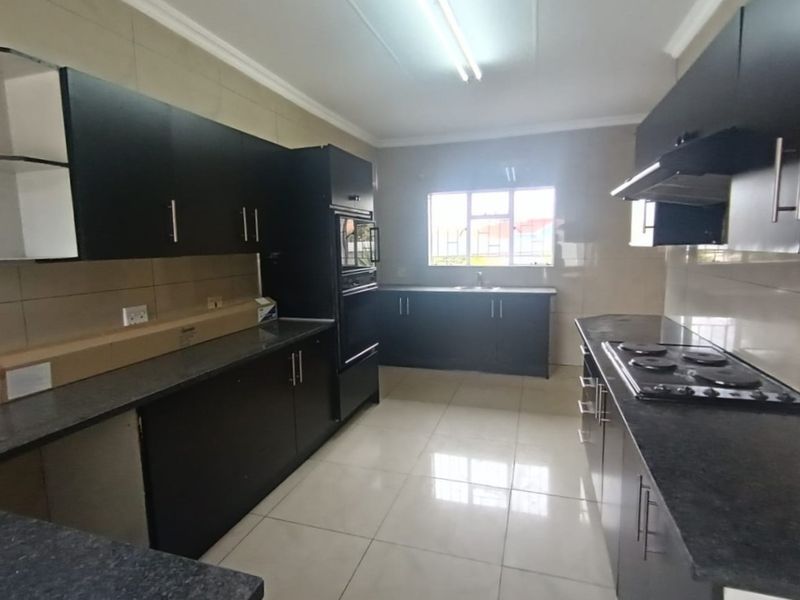 A spacious, modern kitchen featuring dark cabinetry, granite countertops, built-in oven, hob, and extractor fan, with neutral tiled flooring and backsplash.