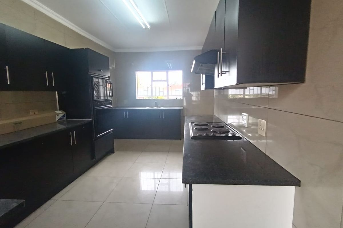 A spacious, modern kitchen featuring dark cabinetry, granite countertops, a built-in oven, hob, and extractor fan, complemented by neutral tiled flooring and backsplash.
