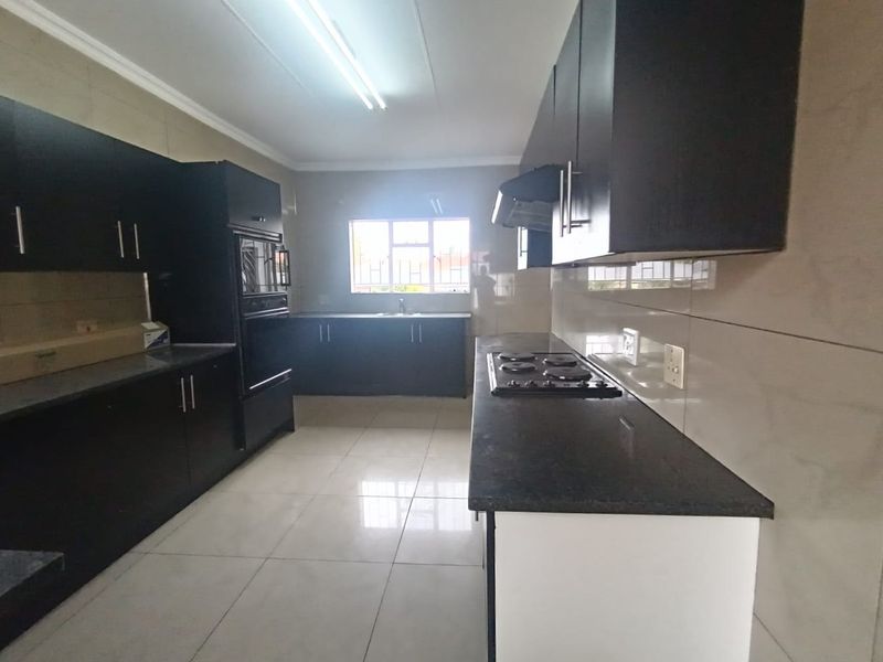 A spacious, modern kitchen featuring dark cabinetry, granite countertops, a built-in oven, hob, and extractor fan, complemented by neutral tiled flooring and backsplash.