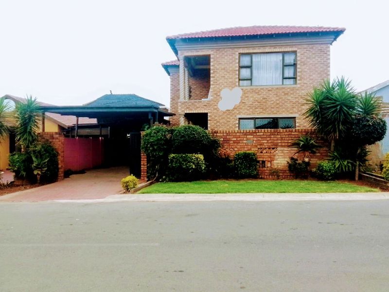 Front view of a two-story face brick house featuring a carport, paved driveway, and boundary wall, with visible unfinished exterior elements.