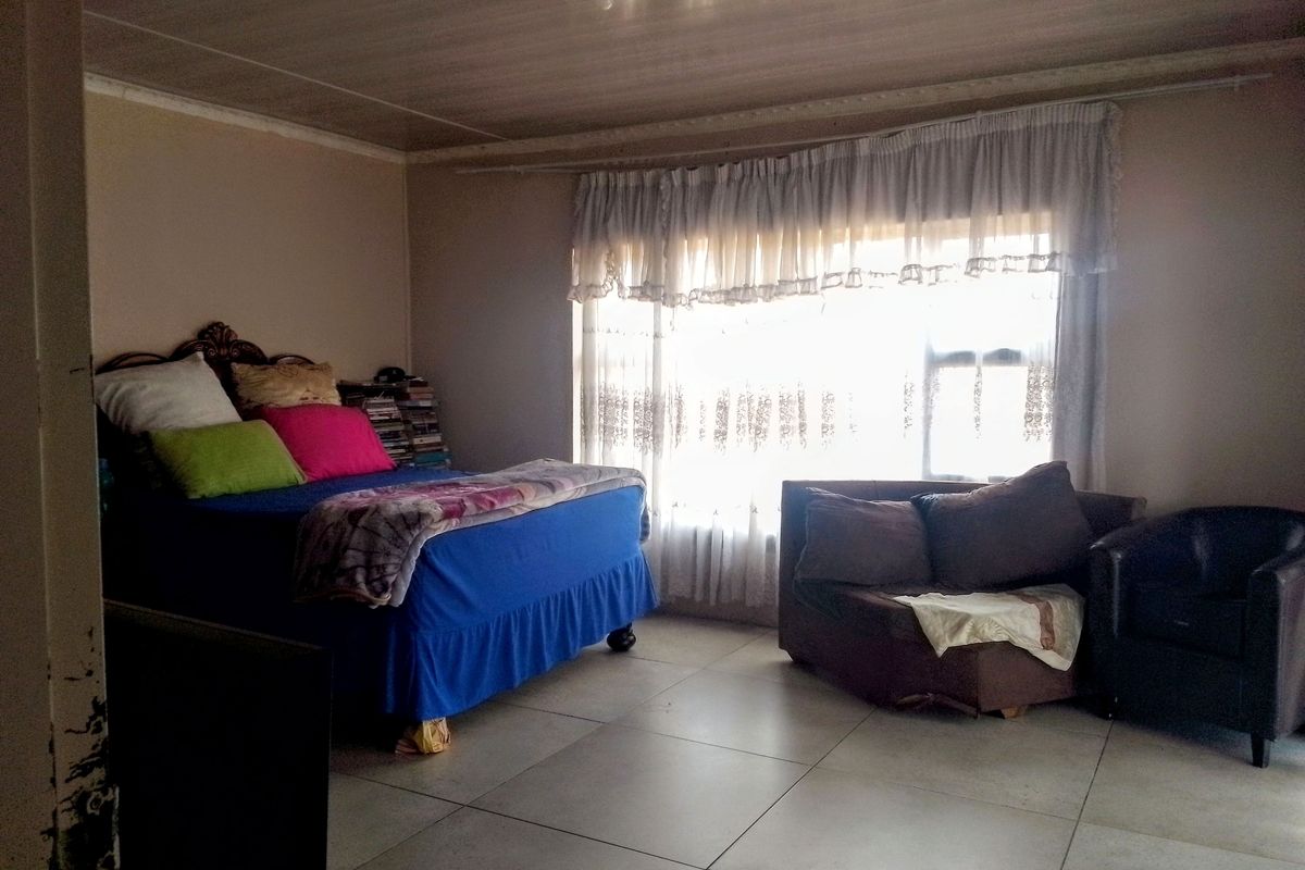 A spacious bedroom featuring large windows with natural light and tiled flooring, offering a blank canvas for potential interior updates and modernization.