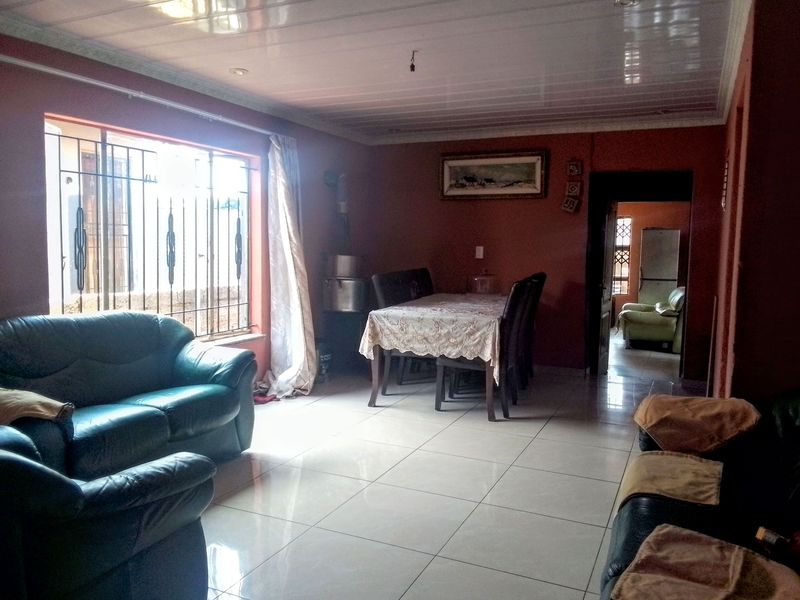 Open plan living and dining area featuring tiled flooring, security bars on windows, and glossy ceiling panels.