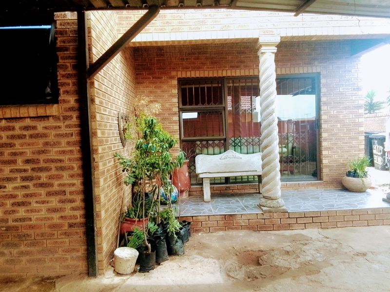 A covered patio area featuring brick walls, a decorative column, and tiled flooring, providing a functional outdoor space for relaxation.