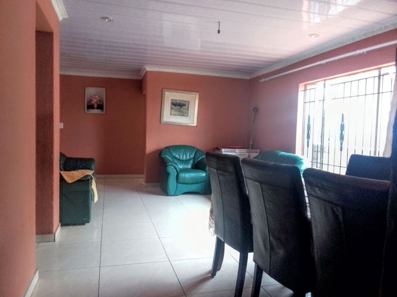 A living area featuring tiled flooring, coved ceilings with recessed lighting, and security bars on the windows.