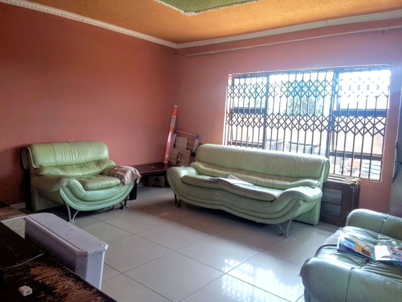 A living room featuring tiled flooring, decorative ceiling cornices, and a window fitted with a security gate.