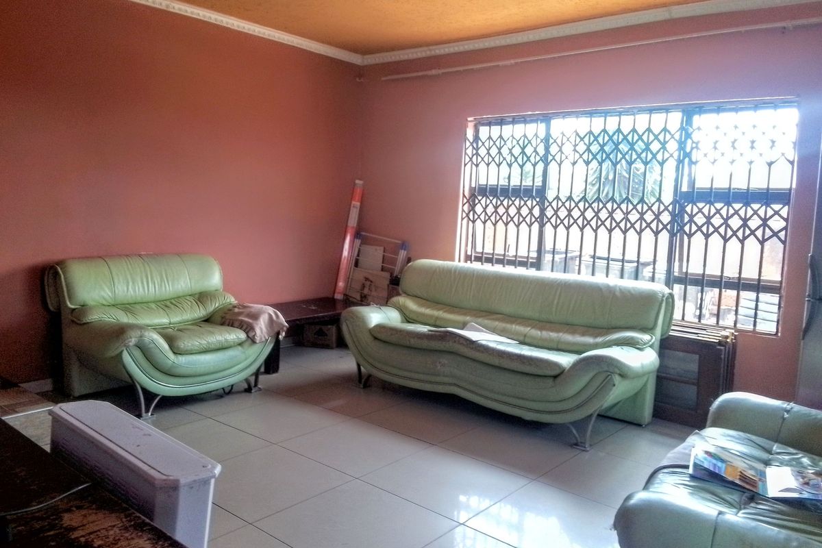 A living room featuring tiled flooring, decorative ceiling cornices, and a window fitted with a security gate.