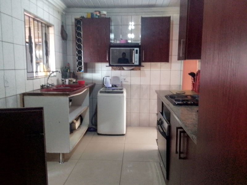 A functional kitchen featuring dark wood cabinetry, built-in oven and hob, tiled splashbacks, and a stainless steel sink with security bars on the window.
