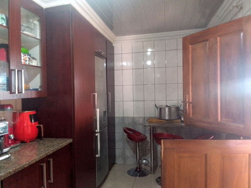A compact kitchen featuring dark wood cabinetry, granite countertops, and a tiled splashback with a tongue and groove ceiling finish.