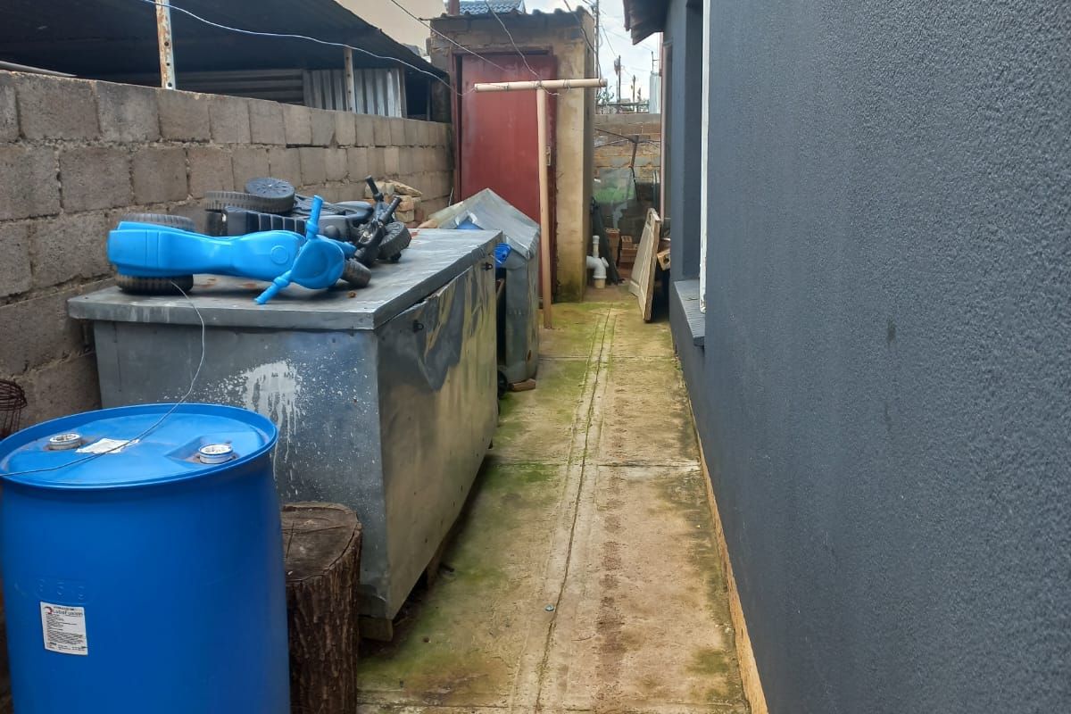 A narrow side passage featuring concrete paving and a plastered exterior wall, showing signs of wear and surface staining.
