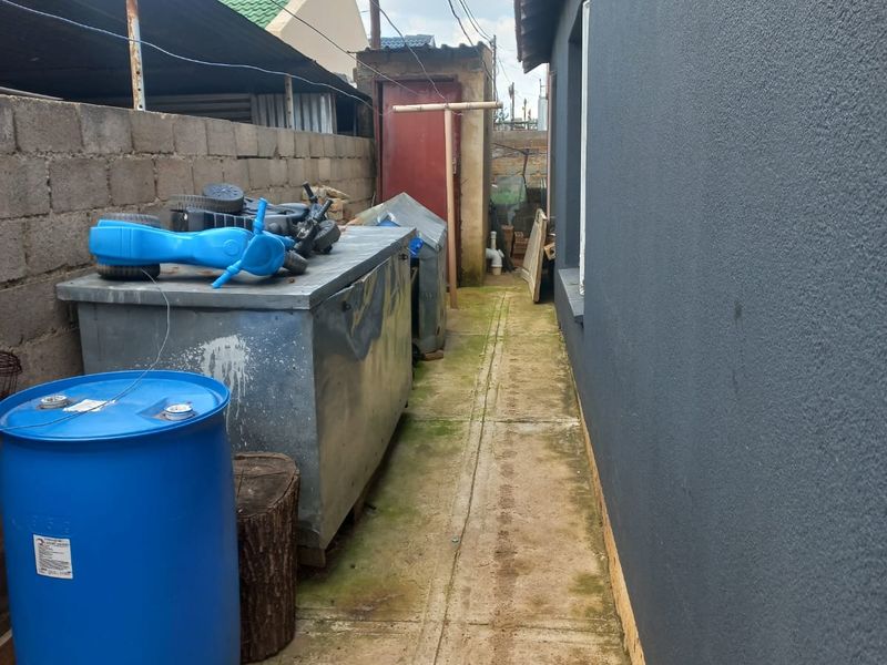 A narrow side passage featuring concrete paving and a plastered exterior wall, showing signs of wear and surface staining.