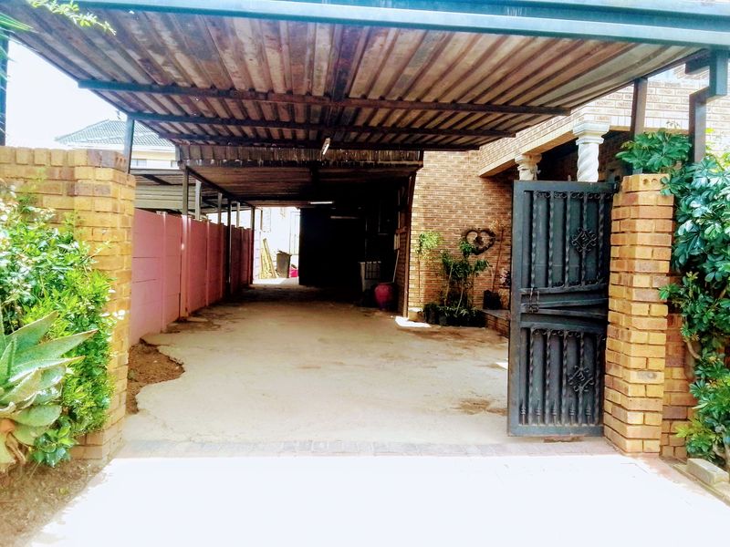 A covered carport area featuring a corrugated metal roof, brick pillars, and a secure wrought iron gate entrance.