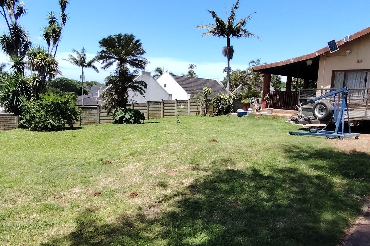 A spacious rear garden featuring a lawn area, perimeter boundary wall, and a covered patio attached to the main house structure.