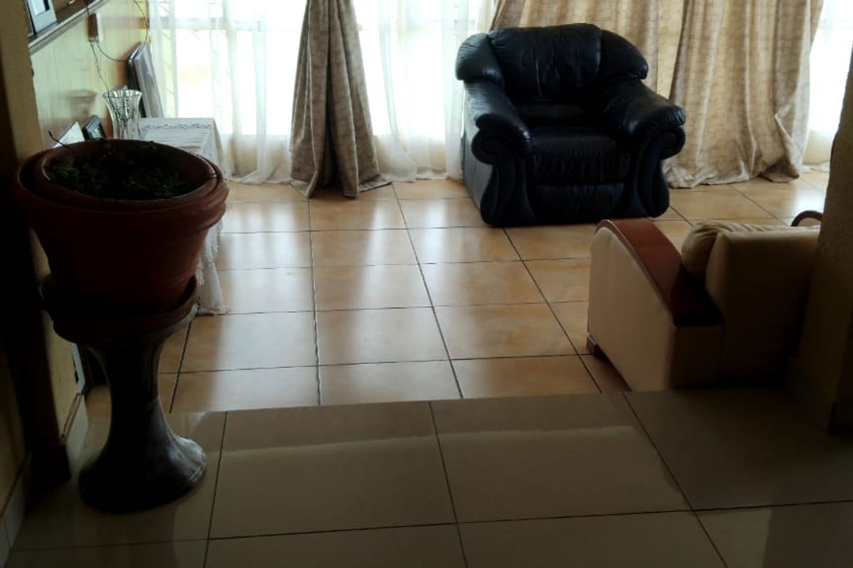 A living room area featuring tiled flooring and large windows that provide natural light.