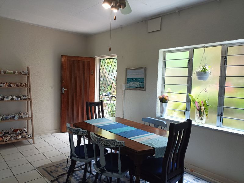 A dining area featuring tiled flooring, a timber door with a security gate, and aluminium windows with burglar bars.
