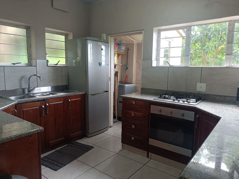 Functional kitchen featuring granite countertops, wooden cabinetry, built-in oven, gas hob, and tiled flooring with access to a separate scullery area.