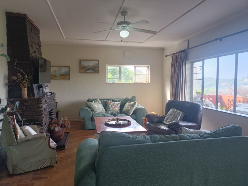 A spacious living room featuring a prominent stone fireplace, parquet flooring, and large windows that provide natural light and scenic views.