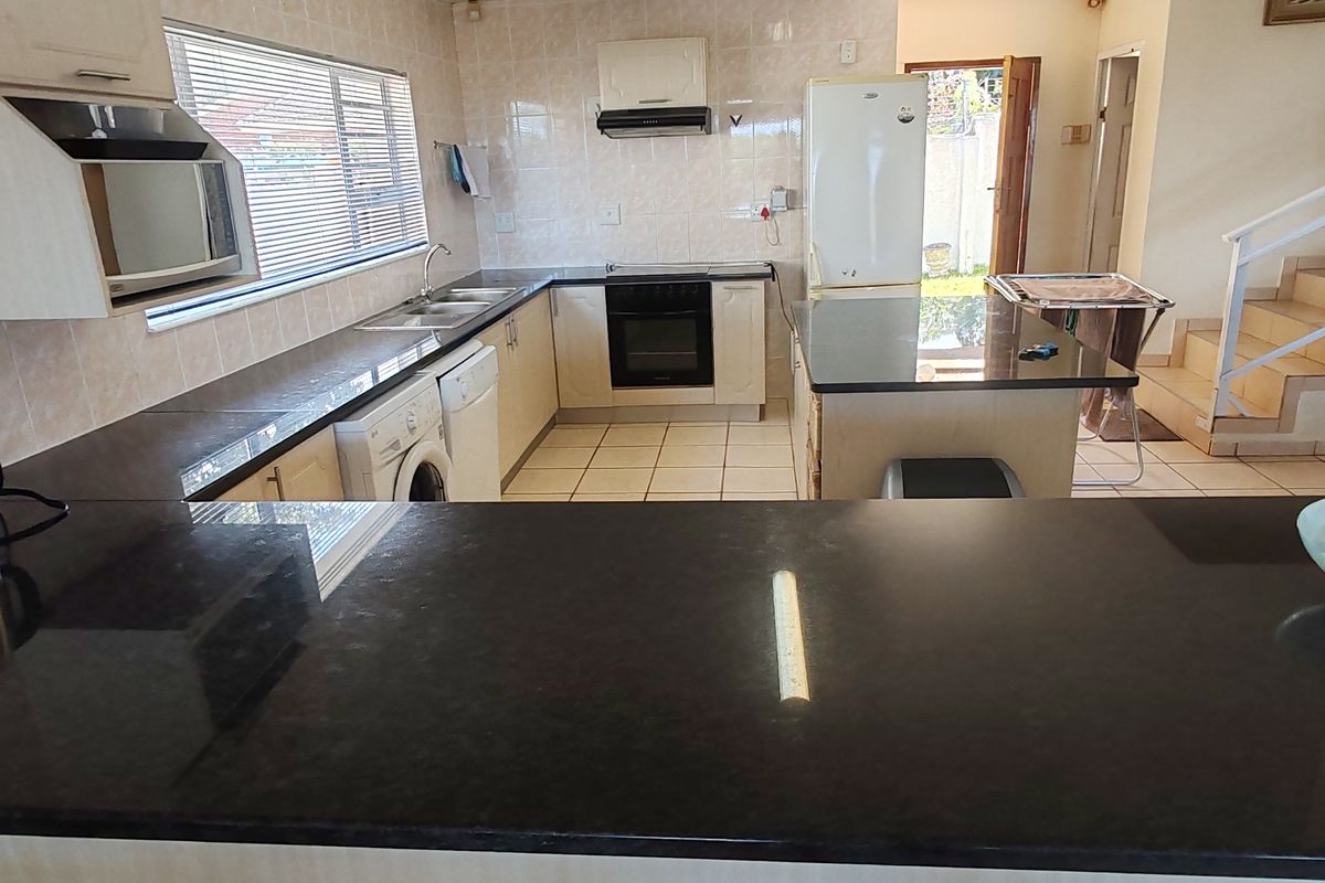 Functional kitchen featuring dark granite countertops, built-in oven, extractor fan, and tiled splashbacks, with an open-plan layout leading to the staircase.