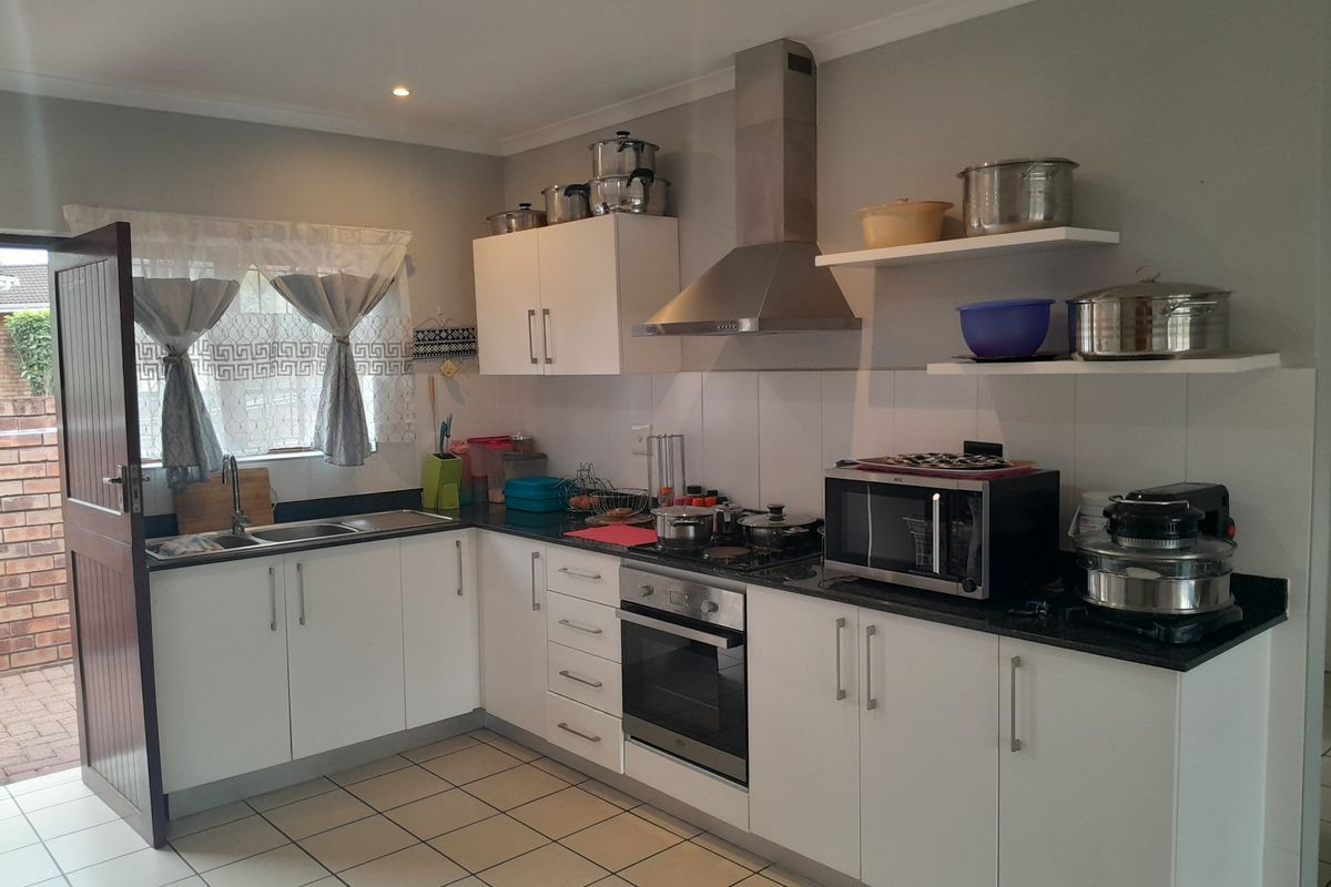 A functional kitchen featuring white cabinetry, dark granite countertops, a built-in oven, gas hob, and stainless steel extractor fan with tiled flooring.