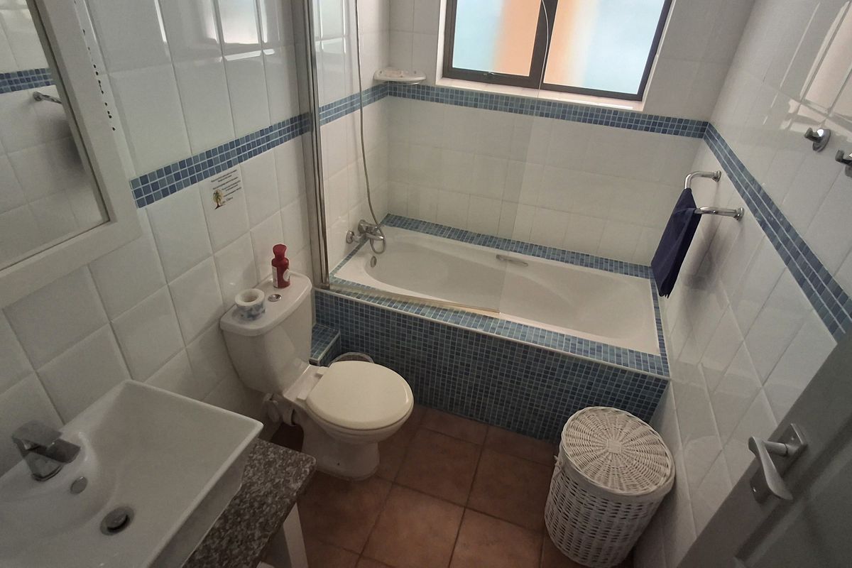A compact bathroom featuring a built-in bathtub with shower mixer, a pedestal basin, and a standard toilet, finished with tiled walls and flooring.