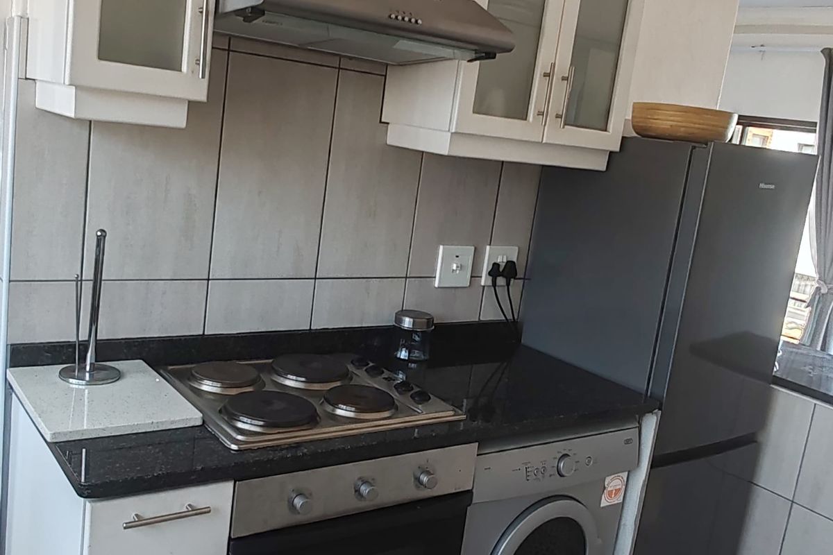 Compact kitchen featuring white cabinetry, granite countertops, built-in oven and hob, extractor fan, and tiled flooring.
