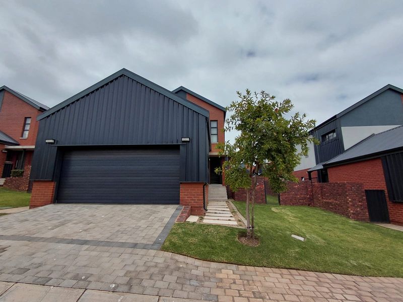 Modern front elevation featuring a double garage with dark metal cladding, brick accents, a paved driveway, and a landscaped front garden.