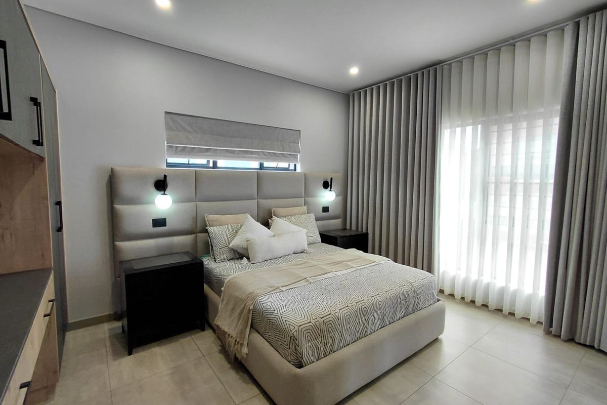 Modern bedroom featuring a large upholstered headboard, integrated wall lighting, floor-to-ceiling curtains, and neutral tiled flooring.