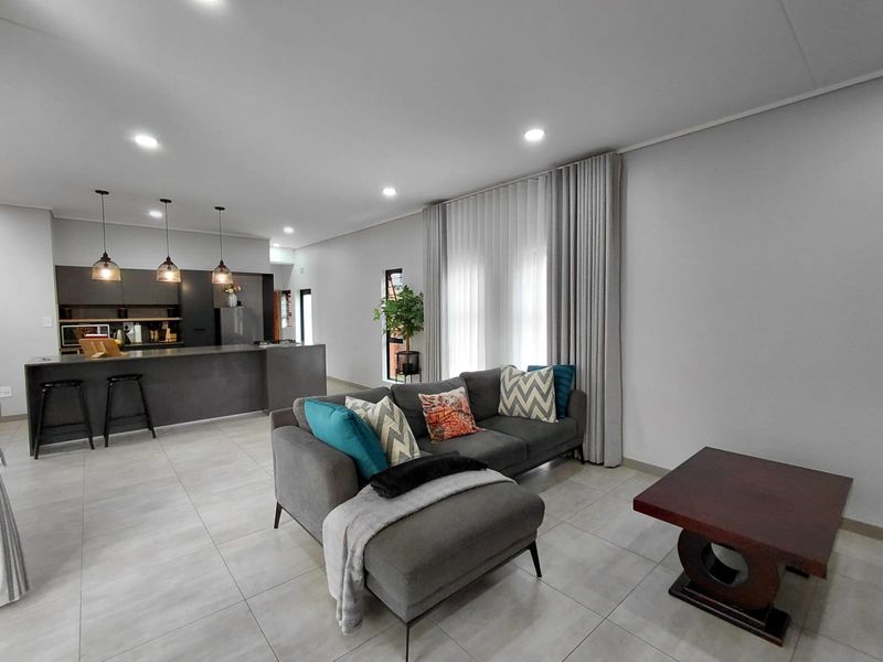 Modern open-plan living area featuring a sleek kitchen island, neutral tiled flooring, and recessed lighting, creating a bright and cohesive space.