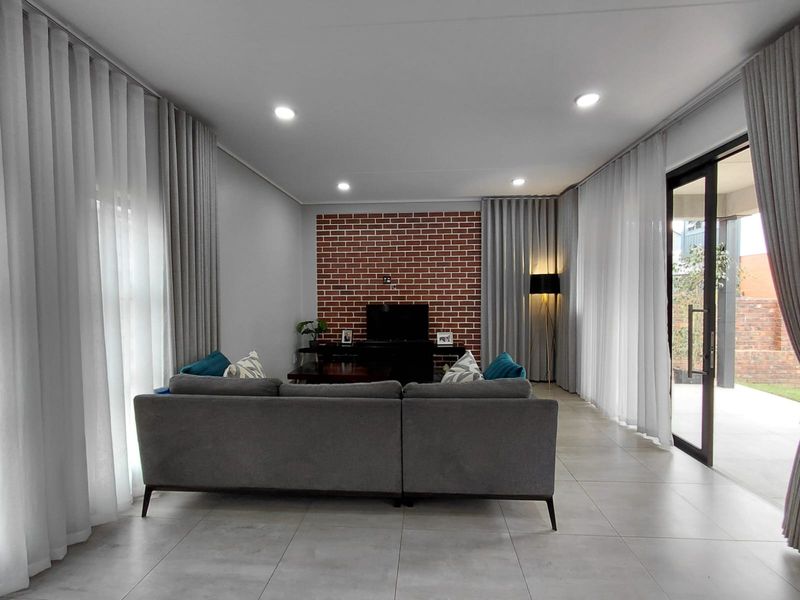 Modern living room featuring a striking exposed brick feature wall, large format floor tiles, and expansive glass sliding doors leading to the outdoor area.