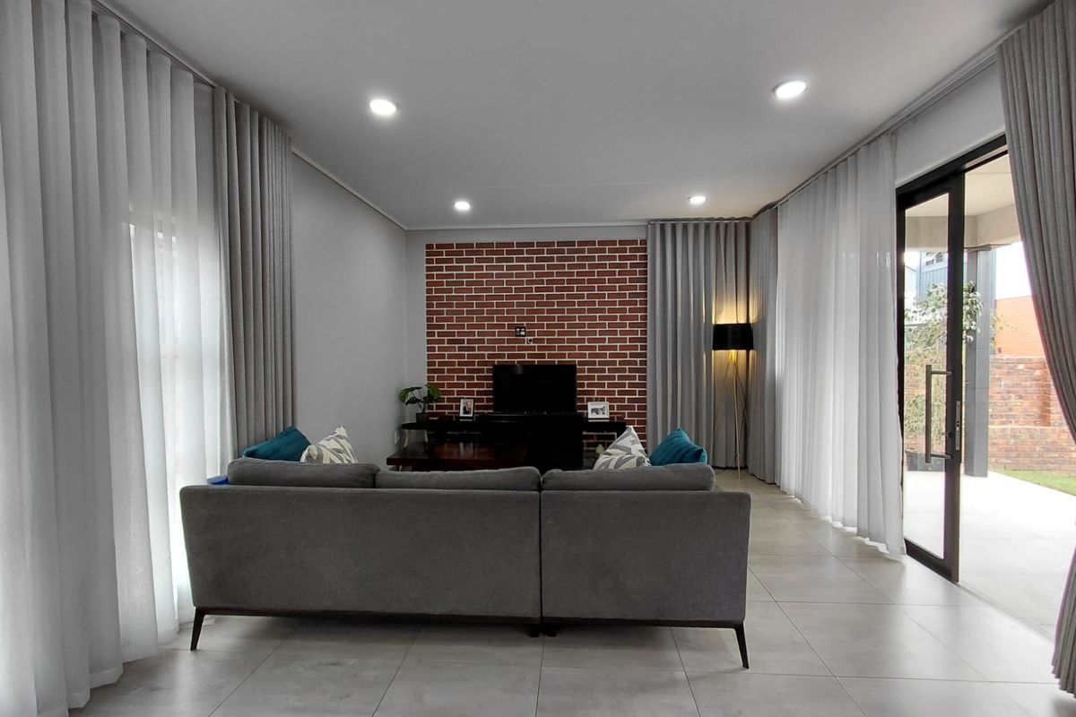 Modern living room featuring a striking exposed brick feature wall, large format floor tiles, and expansive glass sliding doors leading to the outdoor area.