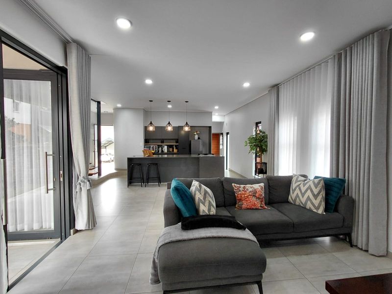 Modern open-plan living area featuring a sleek kitchen island, tiled flooring, recessed lighting, and large sliding glass doors leading to the outdoors.