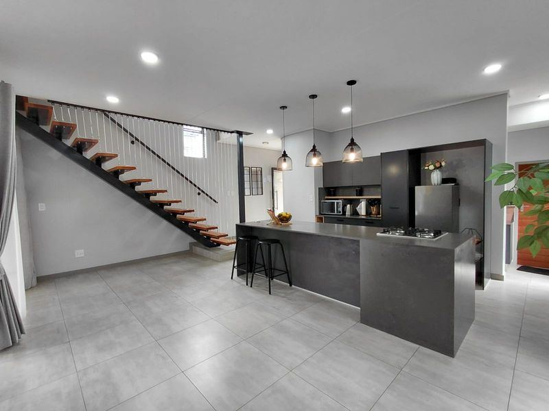 Modern open-plan kitchen featuring a large island with a gas hob, sleek cabinetry, and a striking floating staircase with cable balustrades.