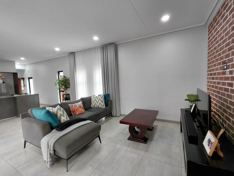 Spacious open-plan living area featuring modern tiled flooring, recessed downlighting, and a stylish exposed brick feature wall.