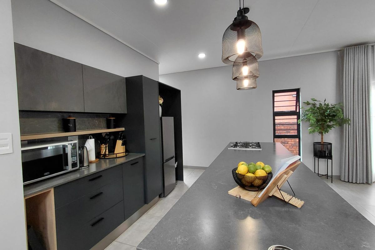 Modern kitchen featuring dark cabinetry, a large central island with a gas hob, stone countertops, and stylish pendant lighting.