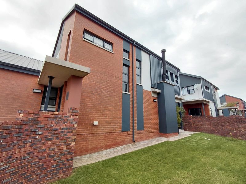 A modern two-story house exterior featuring a combination of red brick and dark metal cladding, with a paved walkway and landscaped lawn.