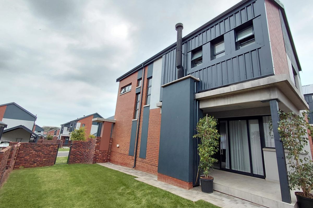 Modern two-story residence featuring a combination of brick and metal cladding, a covered patio area, and a private rear garden.