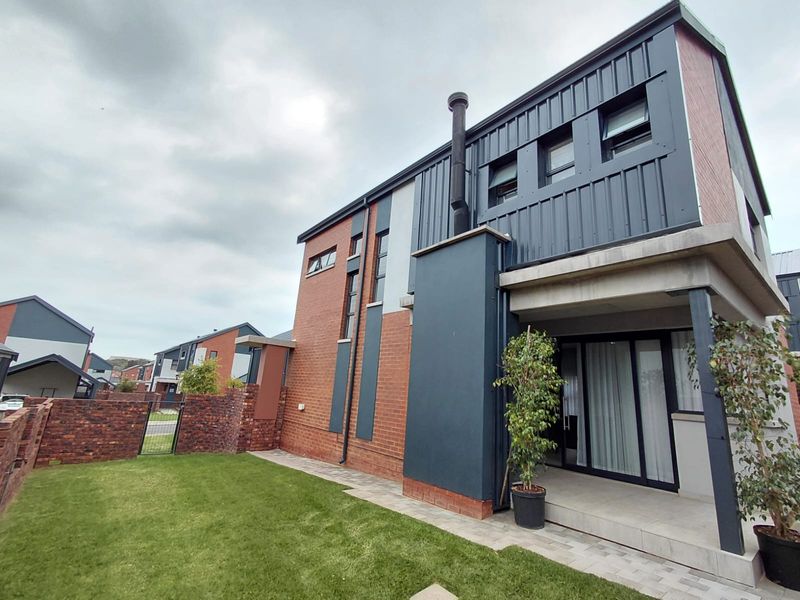 Modern two-story residence featuring a combination of brick and metal cladding, a covered patio area, and a private rear garden.