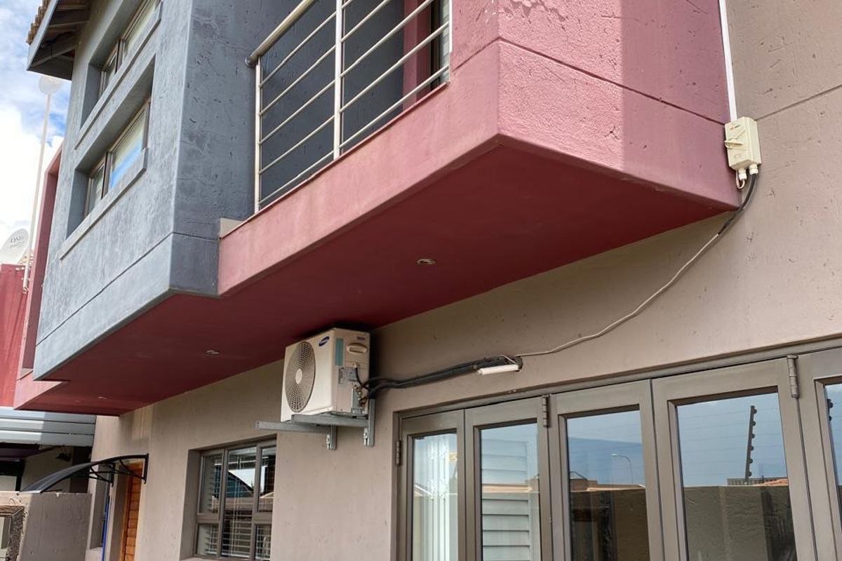 Rear elevation of the townhouse featuring a balcony with stainless steel balustrades, aluminium stacker doors, and an installed air conditioning unit.