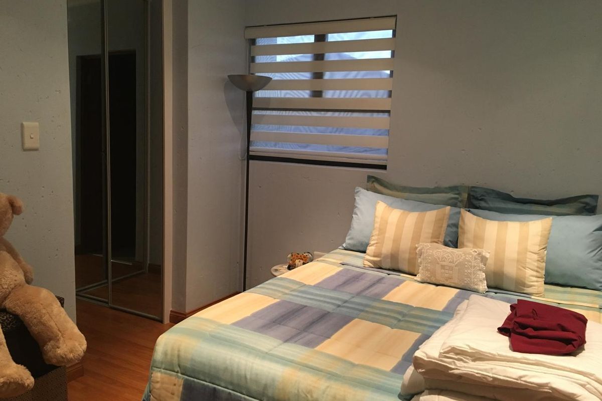 A bedroom featuring laminate flooring, a built-in mirrored wardrobe, and a window fitted with a modern roller blind.