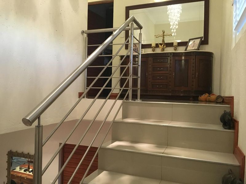 A bright hallway featuring a modern stainless steel balustrade and tiled staircase leading to an upper landing area.