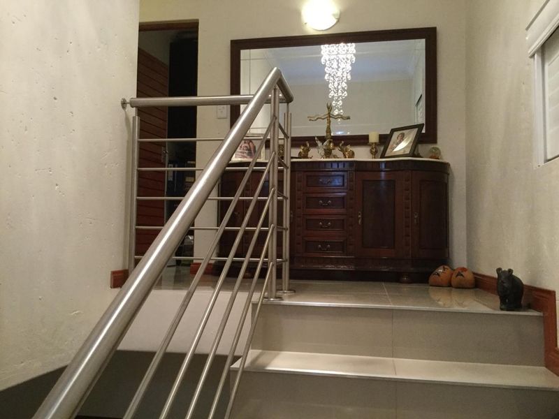 A well-maintained hallway featuring a modern stainless steel balustrade and tiled staircase leading to an upper landing area.