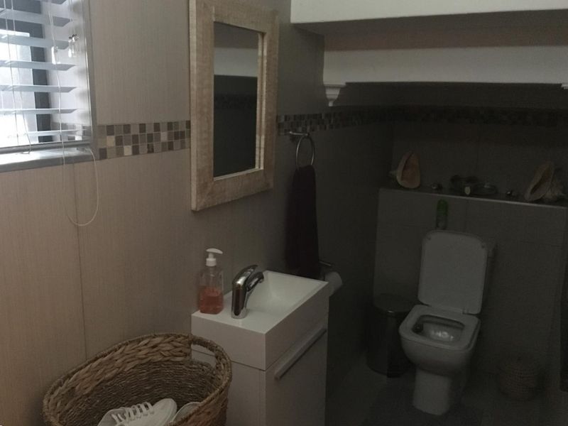A compact bathroom featuring a modern wall-mounted vanity, basin, and toilet with neutral wall tiling and a mosaic accent border.